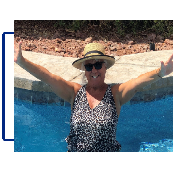 A woman in a hat and sunglasses is standing by the pool.
